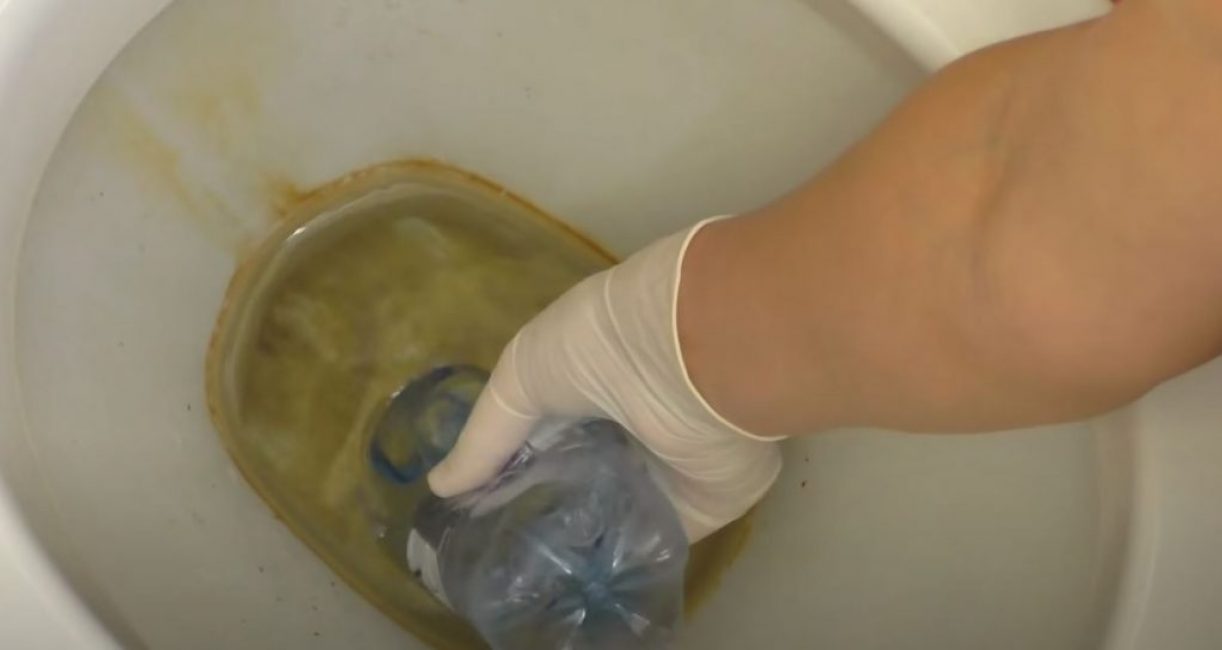 Spremendo una bottiglia di plastica, abbassa il collo nella toilette